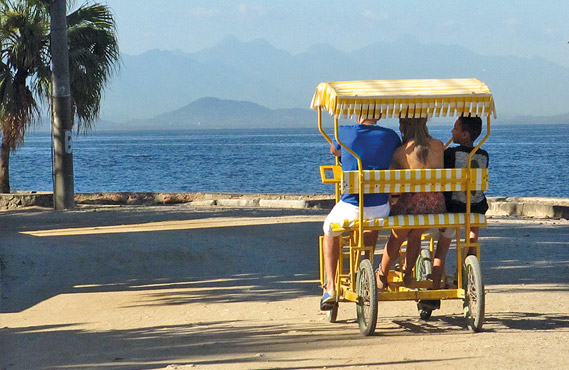 um casal e uma criança em um triciclo amarelo, próximo a ilha dos lobos